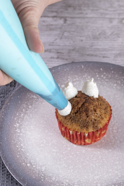 女人的手用挤花袋添加奶油到纸杯蛋糕。自制糕点烹饪概念。垂直照片和选择焦点图片下载