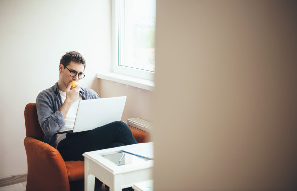 一个戴眼镜的高加索人正坐在笔记本电脑前吃着苹果图片下载