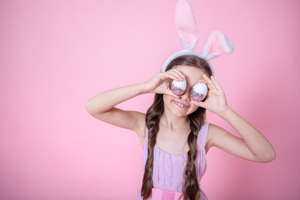 一个漂亮的小女孩穿着复活节兔子耳朵和摆姿势与复活节彩蛋复制空间。图片下载