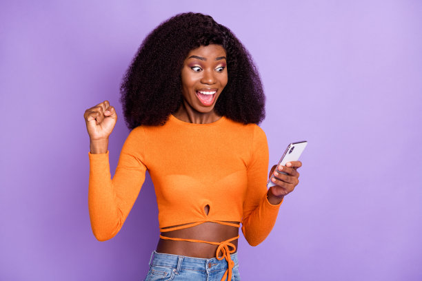 照片迷人的印象深刻的深色皮肤的女人穿着橙色的露脐上装看起来小玩意升起的拳头孤立的紫色背景图片下载