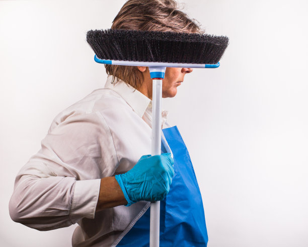 一位戴着蓝色橡胶手套、系着围裙的妇女正拿着扫帚准备出发。图片下载