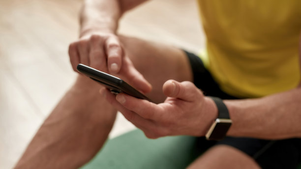 健身应用程序。一个男人坐在家里的瑜伽垫上使用智能手机的剪发照片图片下载