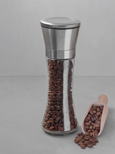 在灰色的背景下，一个银色盖子的高玻璃罐里装着咖啡豆。本空间图片下载