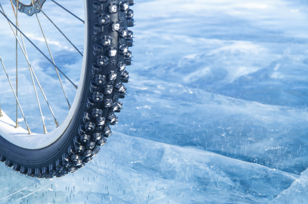 一个有钉的自行车轮胎的特写在一个结冰的表面的背景上。冬季运动的概念。自行车在冰上。图片下载