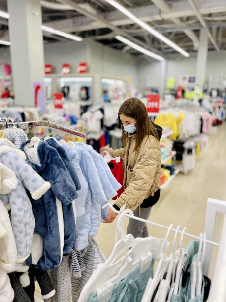 年轻妇女戴着医用口罩在婴儿商店为孩子买衣服图片下载