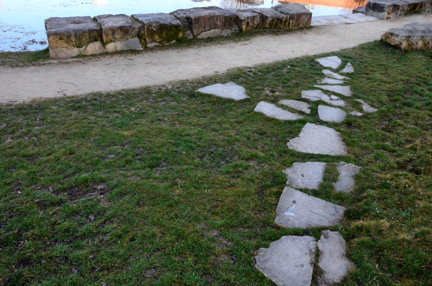 池塘边的休闲区有一个公园里的石头楼梯，是由米色砂岩制成的石阶小径。前景是草坪上由一块块平坦的石头铺成的人行道图片下载