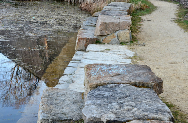 池塘边的休闲区有一个公园里的石头楼梯，是由米色砂岩制成的石阶小径。前景是草坪上由一块块平坦的石头铺成的人行道图片下载
