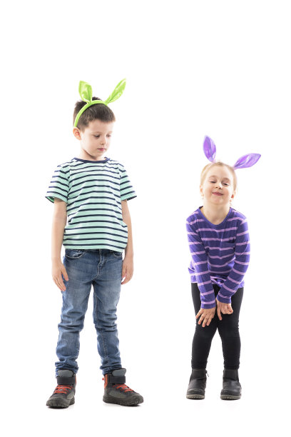 困惑的复活节男孩看着调皮的女孩做着兔子耳朵的脸。图片下载