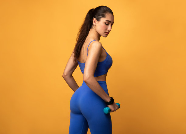 在橙色背景下手持哑铃摆姿势的运动型女人图片下载