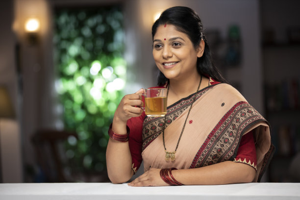 一个中年妇女喝绿茶站在窗户和阳台:-库存照片图片下载