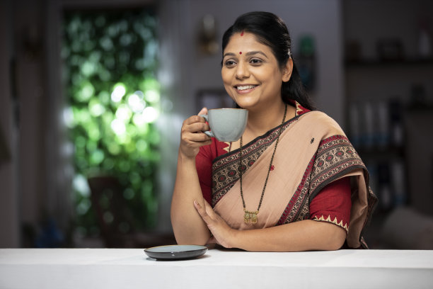 一个中年妇女喝咖啡站在窗户和阳台:-库存照片图片下载