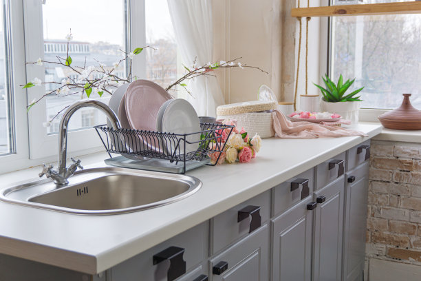 厨房水槽的侧视图，花和盘子靠近窗户在阴天图片下载