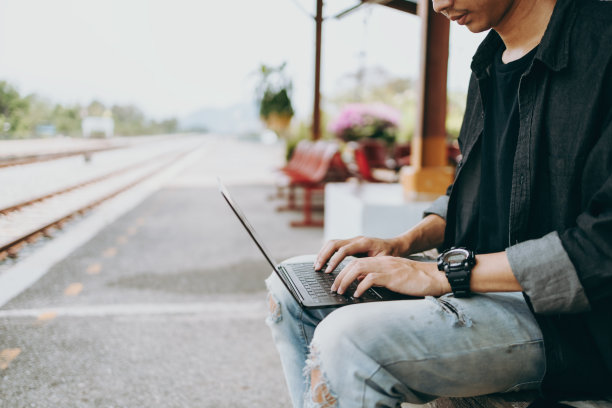年轻的亚洲人使用笔记本电脑工作和搜索位置的旅行在火车站。自由职业者工作和旅行的概念。图片下载