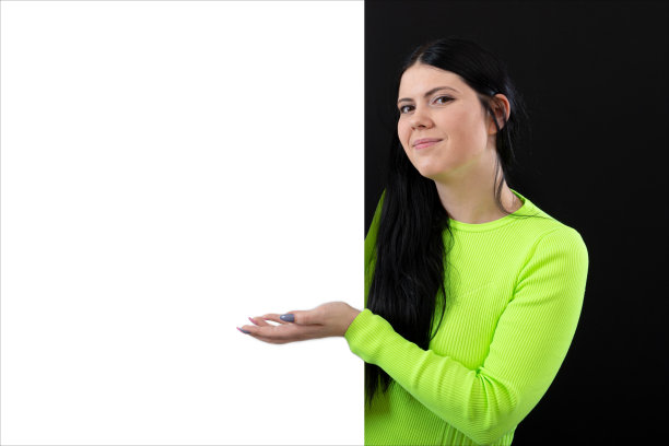 迷人的黑发女子在鲜艳的衣服与白色空白海报，孤立在一个黑暗图片下载