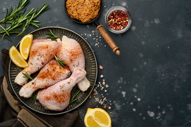 生鸡腿和烹饪材料在黑色的石头背景。食物背景，生肉与香料在黑色的桌子。前视图。图片下载