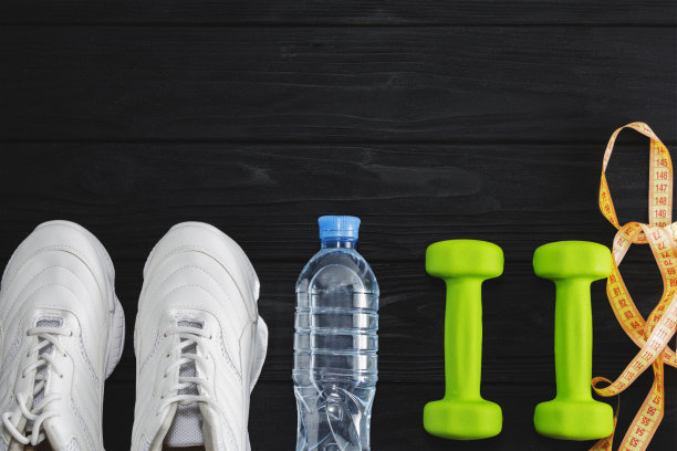 黑色背景上有哑铃和一瓶水的跑鞋。健康的生活方式图片下载