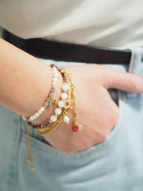 手镯堆积在一个女人手上的一条牛仔裤，粗斜纹棉布裤子。镶有珠子和黄金的手镯。图片下载