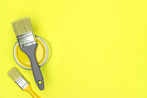 两个画笔和封闭的黄色油漆罐照亮黄色背景。房子装修。图片下载