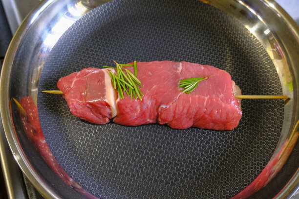 生红肉串在煎锅上与迷迭香俯视图。烹调肉类图片下载