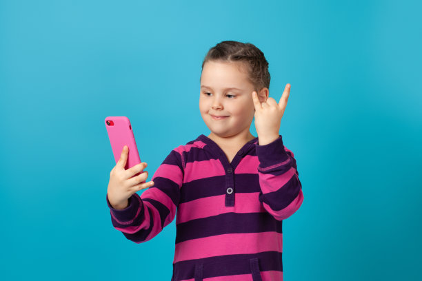 特写的微笑可爱的女孩与马尾辫在视频聊天电话，显示她的手指角的迹象，孤立在蓝色的背景图片下载