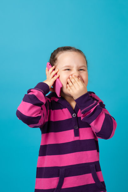扎着辫子的女孩的肖像，笑到哭打电话和她的嘴与她的手从笑，孤立在一个蓝色的背景图片下载