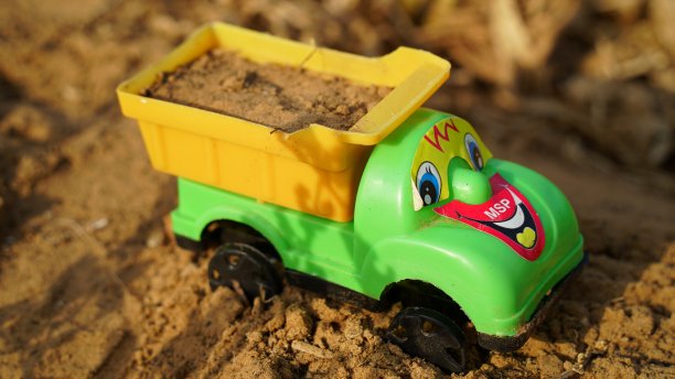 玩具用黄色的手推车装满了泥土。儿童玩工具的特写。童年的玩具，绿色的卡车和手推车袋。图片下载