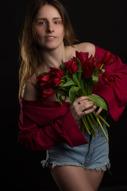 一名年轻女子的画室肖像，背景为黑色，手里拿着一束红色郁金香图片下载
