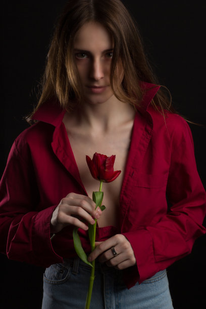 一名年轻女子的画室肖像，背景为黑色，手里拿着一束红色郁金香图片下载