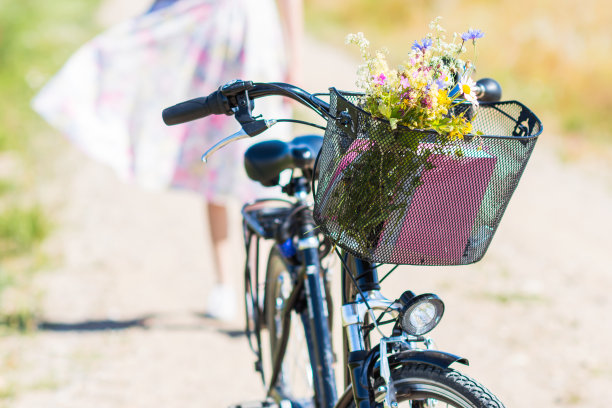 野花花篮中的自行车与女子在鲜花服装的背景，自行车与鲜花在田野在夏季阳光明媚的一天图片下载