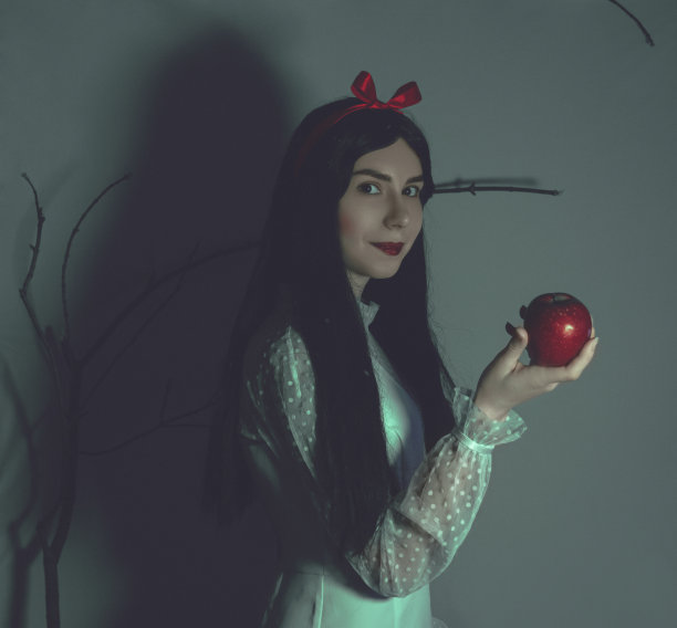 年轻漂亮的女人，白皙的皮肤和红润的嘴唇，保持着红色有毒的苹果在树枝的背景。扮演白雪公主图片下载