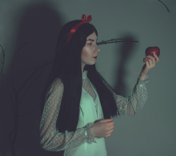 年轻漂亮的女人，白皙的皮肤和红润的嘴唇，保持着红色有毒的苹果在树枝的背景。扮演白雪公主图片下载