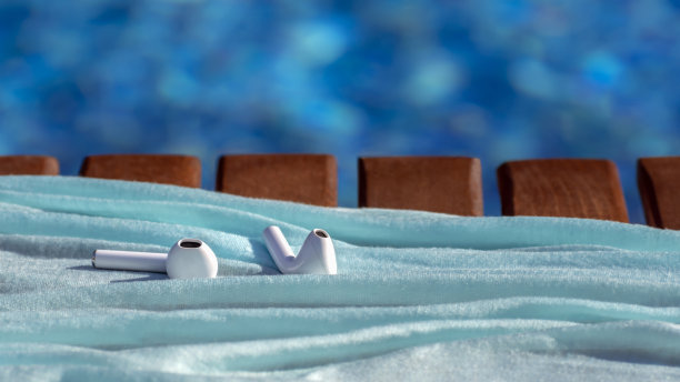 白色无线耳机-蓝牙耳机或耳机躺在游泳池附近与蓝色的水。在运动、放松和娱乐中使用现代科技设备。本空间图片下载