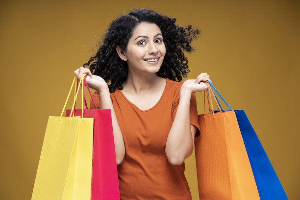 肖像的年轻女子提着购物袋站在孤立的黄色背景:-库存照片图片下载