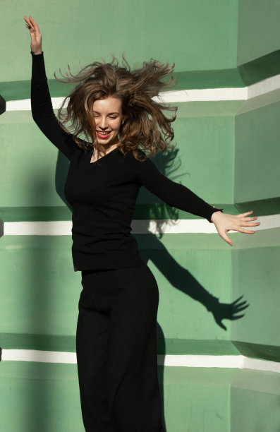 在绿色墙壁的背景下，一个穿着时尚套装的长发女孩的剪影图片下载