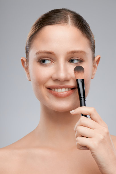美丽的年轻女士拿着化妆刷和摆姿势在工作室。美摄影图片下载