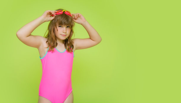 一个美丽的十几岁的女孩穿着粉红色的彩色游泳衣准备在游泳池游泳。模型。在绿色背景下，穿着鲜艳泳衣和眼镜的有趣的孩子。文本的地方图片下载