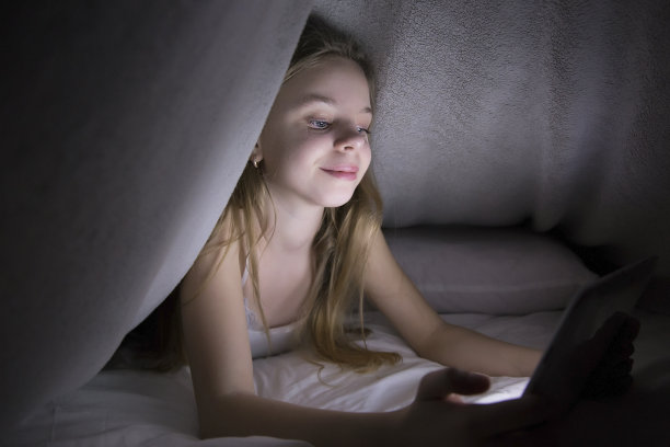 孩子，可爱的女孩，在平板电脑上听音乐和玩游戏，晚上在毯子下，躲着父母图片下载
