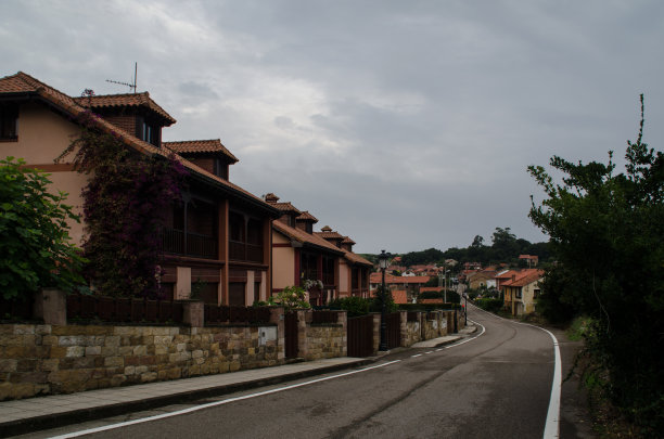 弯弯曲曲的道路穿过一个城镇，旁边有漂亮的房子。西班牙坎塔布里亚阴天有雨图片下载
