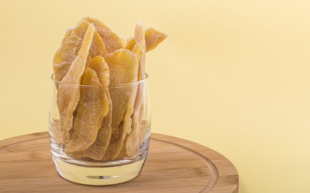 东方糖果干芒果在一个玻璃杯在黄色的背景图片下载