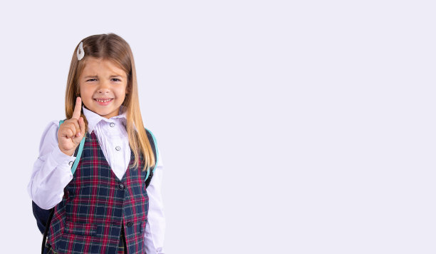一个穿着校服的小学女孩的工作室照片。微笑并向上指。食指向上和外侧空间。灰色背景。图片下载