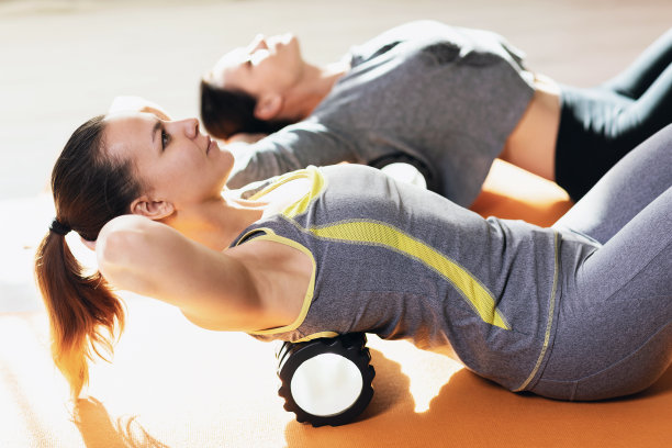 两名妇女穿着运动服，过着健康的生活方式，在体操垫子上使用按摩轮进行背部肌肉的肌筋膜放松图片下载
