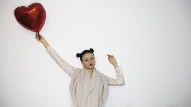 一个女人闭着眼睛，让一个充满爱的气球带着她。文本的负空间或复制空间。图片下载