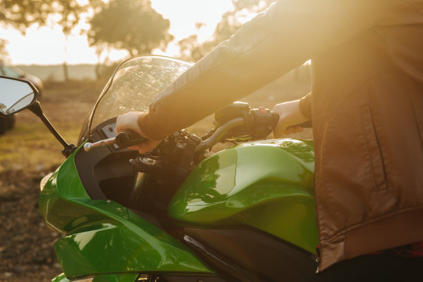 一个穿着棕色皮夹克的摩托车手，在路上骑着他的摩托车，在他前面的太阳创造了一个剪影。图片下载