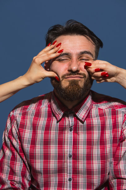 年轻男子的肖像与女性的手打他的脸在蓝色的背景图片下载