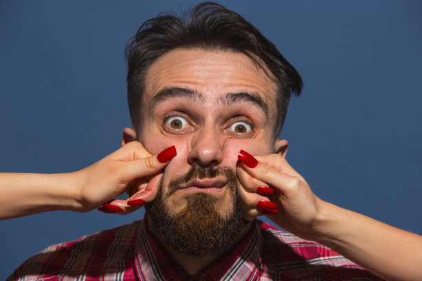 年轻男子的肖像与女性的手打他的脸在蓝色的背景图片下载