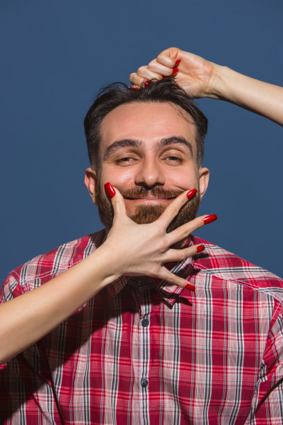 女性的手使年轻的胡子英俊男子在蓝色的背景微笑图片下载