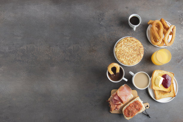 典型的西班牙早餐概念。玉米粉圆饼，意式烤面包配火腿和番茄，油条配巧克力，脆皮吐司配黄油和果酱，咖啡和橙汁。图片下载