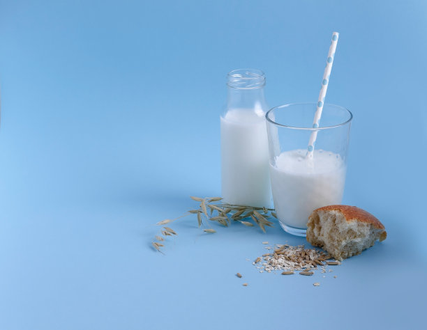 牛奶燕麦片在一个高玻璃和一个管站在蓝色的背景。旁边是一个燕麦糠面包，复制空间，健康食品的概念图片下载