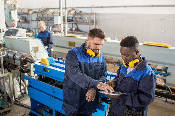 现代工厂两名年轻跨文化男性工人在车间在线讨论技术资料图片下载