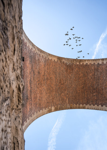 古老的铁路拱形高架桥，由石头和砖组成，从地面俯瞰蓝天。鸟儿从高架桥上起飞鸽子从拱门上飞过。图片下载